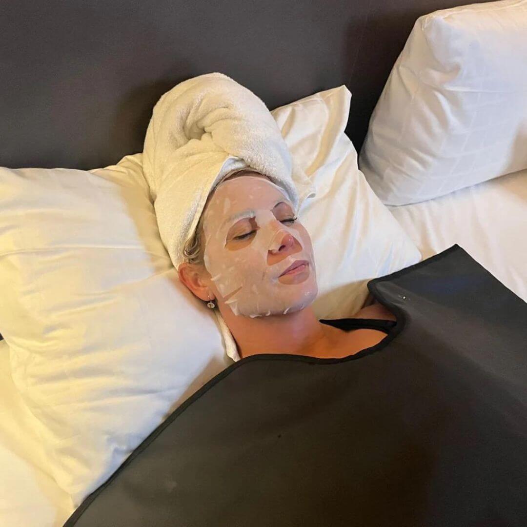 Damer, der nyder Comforth Infrarødt Saunatæppe i hendes seng med ansigtsmaske