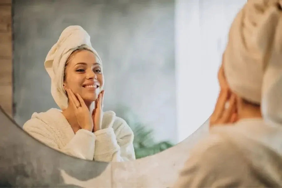 Smilende dame, der kigger sig i spejlet iført badekåbe